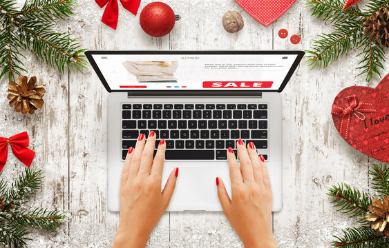 Christmas sale on laptop. Woman shopping on market website. Top view of wooden table with christmas new year decorations, tree and gift.