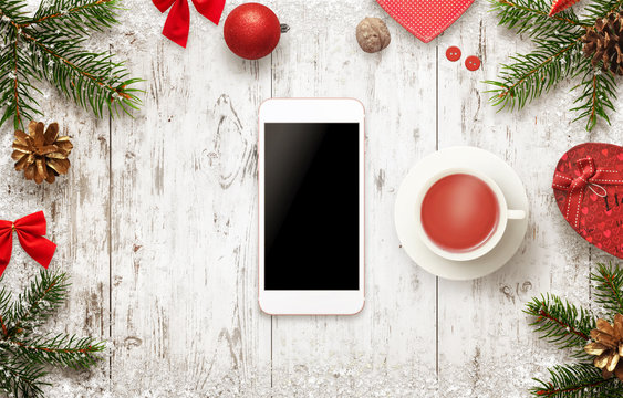 Smart phone with Christmas decorations on table. Drinking tea and a break in the winter days. Isolated display of mobile device for mockup, web site or app presentation.