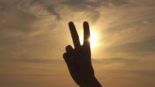 CLOSE UP: Making peace or V sign over stormy sky and golden summer sunshine
