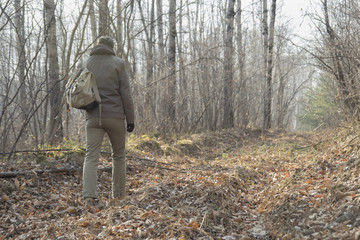 A man in a cap and with a backpack goes on the trail through the woods