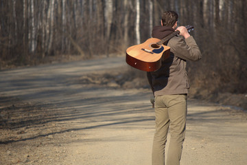 The man with the guitar standing on the road near forest