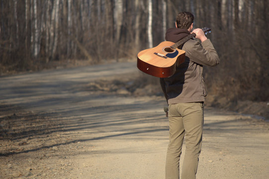 The man with the guitar standing on the road near forest