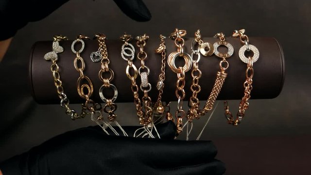 Jewelry in the store, Close-up of a demonstration of gold ornaments hand in a black glove, bangles of yellow and white gold with precious stones, a lot of gold bracelets, chains in the jewelry store