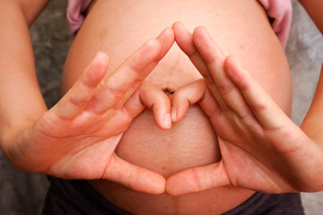 Pregnant Woman holding her hands in a heart shape on her baby bu