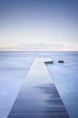 Fototapeta na wymiar Wooden pier, rocks and calm sea on long exposure.