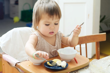 little girl eating in baby sitting, child using fork and spoon 