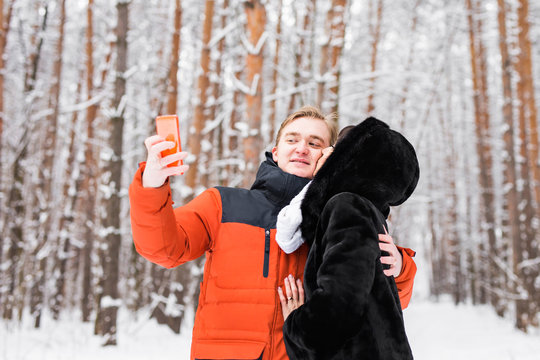 people, season, love, technology and leisure concept - happy couple taking picture with smartphone on over winter background