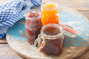 strawberry jam, a fig and apricots in jars on a table, selective focus