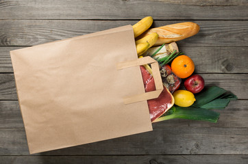 Different food in paper bag on wooden background, close up