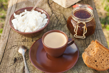 cottage cheese, coffee, jam, milk and bread on a bench in a garden, selective focus