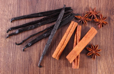 Fragrant vanilla, star anise and cinnamon sticks on wooden surface plank