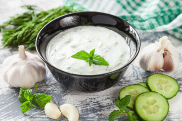 Tzatziki sauce in bowl, with ingredients - cucumber, mint, dill, lemon,  selective focus