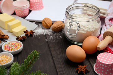 Christmas baking ingredients – muffin molds, spices, butter, eggs and flour on dark wooden background, selective focus, copy space