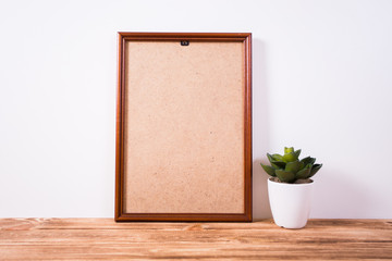 Blank white frame and plant on wooden surface. Mock up
