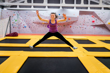 Young sportsman jumping on a trampoline and doing split indoors - obrazy, fototapety, plakaty