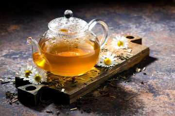 glass teapot of chamomile tea on dark background