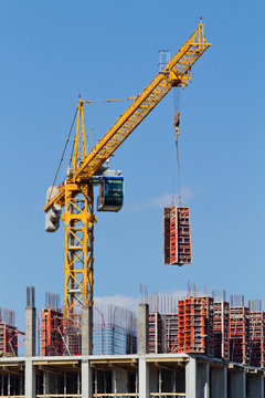 Yellow construction tower crane and house under construction