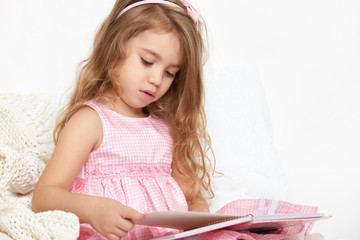 girl child rad book in bed, dressed in pink