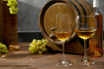 Glasses of white wine, grapes, box and barrel on a wooden table