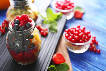 Fresh fruits and berries in glass jar on cutting board