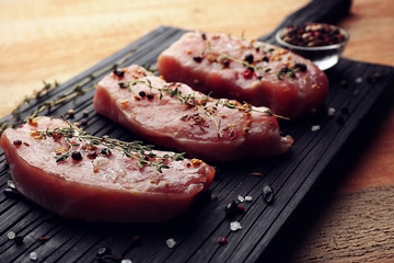 Raw steaks with herb and spices on wooden cutting board