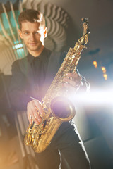 A young man in a suit standing with a saxophone musical instrument