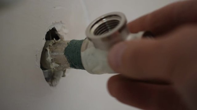 Closeup of plumber screwing up manually a pipe T-joint fitting connector onto pipe end in wall with hemp and sealant threat