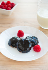 Sticky chocolate cookies with fresh raspberries and a glass of milk on wooden background.