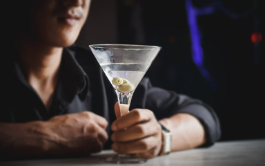 A young man sitting in a bar drinking a martini.