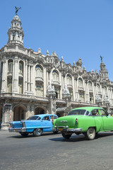 Brightly colored vintage American cars pass in front of the landmark architecture of the Great Theater of Havana, Cuba