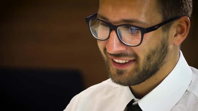 Young male businessman in a white shirt and glasses, working at a computer in the office.