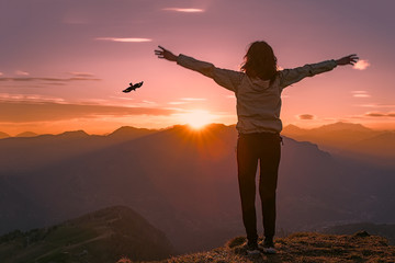 Woman on top of a mountain at sunset looks eagle