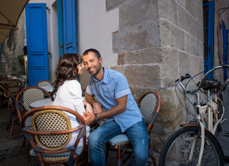 Young romantic couple sitting in sidewalk cafe near their tandem bike. Wife tenderly looking at her husband, he smiles looking at the camera. Lviv, Ukraine