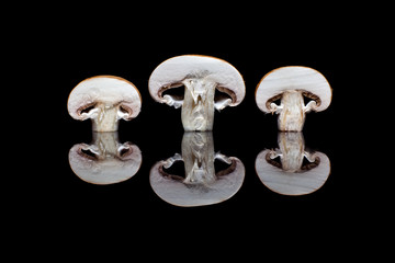 Three halved fresh brown champignons in row isolated on black reflective background