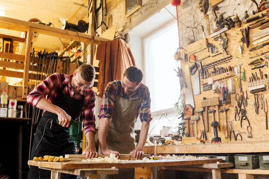carpenters with drill drilling plank at workshop