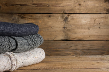 Stack of knitted winter clothes on wooden background.