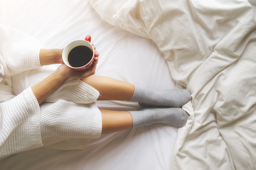 Beautiful asian woman hand holding a cup of coffee on the bed with morning light. Relaxing concept. Retro filter effect,soft focus,selective focus...