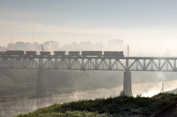 Freight train traveling on the railway bridge over the river foggy morning. Grodno, Belarus.