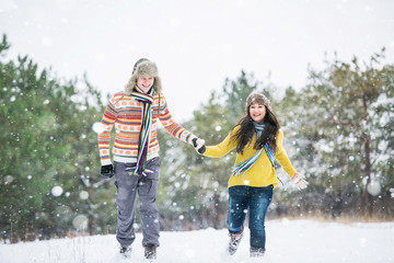 Loving couple in the winter park. Man and woman dressed in sweaters and scarves, winter hats. Snowfall in the forest, holidays, travel.