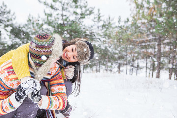 Happy couple in love in the park. Man and woman dressed in a sweater and warm hats, mittens. Snowfall. Trees in the snow, winter forest. Emotional people. Bright multi-colored sweater.