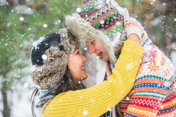 Couple in love walking in the winter woods. Pine Forest, spruce trees. Happy man and a woman. People dressed in sweaters and hats. Emotional people. Snowfall.