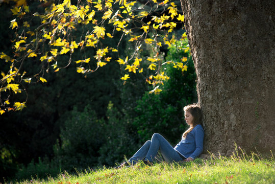 Girl sitting on the grass under a maple tree in autumn