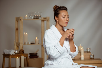 Young beautiful girl holding tea cup relaxing in spa salon.