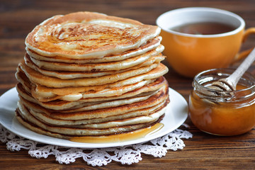 Stack of delicious, homemade pancakes with honey on white plate on wooden background. Healthy breakfast, close up. Pancake's Day. High stack of pancakes shallow DOF.