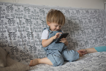 Naklejka premium Toddler boy playing with phone, in light room lifestyle, real in