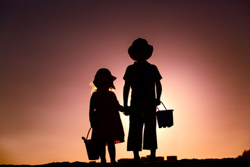Fototapeta na wymiar little boy and girl with beach toys at sunset