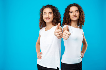 Two pretty girls twins smiling, showing like over blue background.