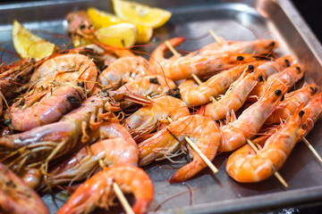 Classic tiger shrimp skewers. Shrimps sriracha kebabs with lemon for dinner. Delicious prawn spit prepared on grill. Extreme close up of appetizing grilled queen prawn on the tray.