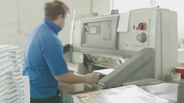 Man works on cutter guillotine machine in a printing factory