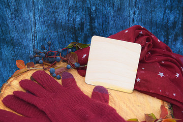Warm burgundy gloves with a scarf and hat on wood background blue color with autumn leaves, and cut down a tree